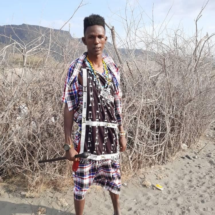 A Maasai man standing on open ground with a walking stick